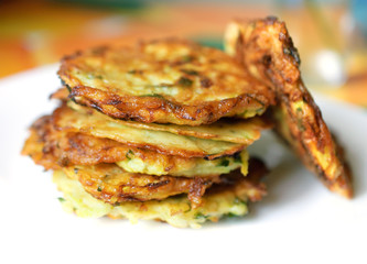 Stack of fried vegetable fritter made of zucchini, eggs, parsley, decorated with a sprig of green onions on a white plate. Selective Focus, Focus on the front of the top fritters