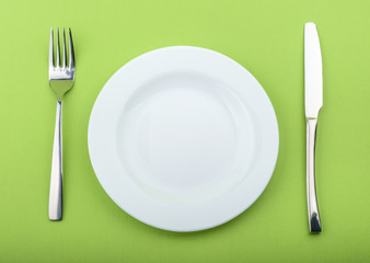 Empty plate, fork and knife on green background