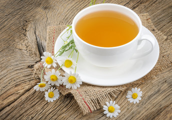 Cup of tea and chamomiles on wooden background