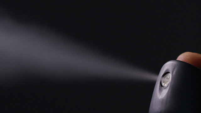 Close up of aerosol can being sprayed against black background, in slow motion at 240fps