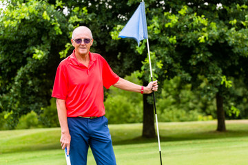 Senior man playing golf on course holding flag