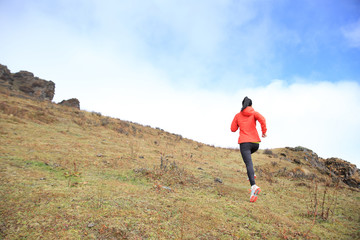 young woman trail runner running on mountain peak