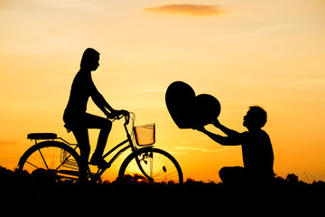 Fototapeta na wymiar a man giving a big heart to a woman riding a bicycle silhouette