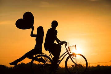 Fototapeta na wymiar Silhouette of a man and a woman riding a bicycle together and holding big hearts