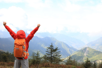 cheering young woman hiker open arms at mountain peak