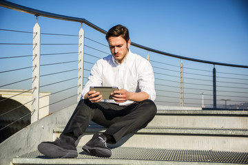 Handsome trendy man looking down at a tablet computer, outdoor