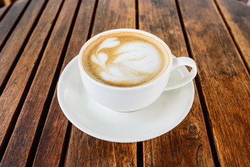  A cup of coffee with leaf pattern in a white cup on wooden background