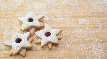 Three star-shaped cookies on a wooden table covered in flour.