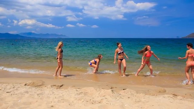 cheerleaders in bikinis perform hand scale stunt on wet sand