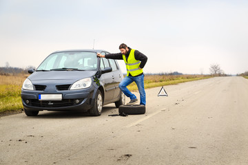 Upset man trying to replace a flat tire by the road.