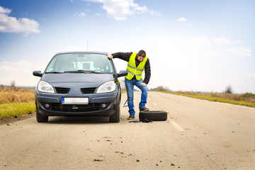 Man having trouble to change a flat tire on his car by the road
