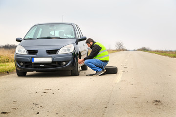 Fototapeta na wymiar Man unscrewing nuts to repair a flat tire by the road