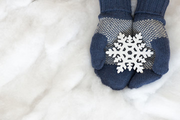 Woman hands in light teal knitted mittens are holding snowflake