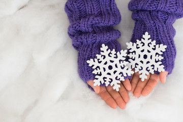 Woman hands in light teal knitted mittens are holding snowflakes