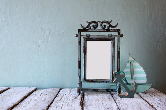 low key image of old victorian steel blue blank frame and wooden sailing boat on wooden table
