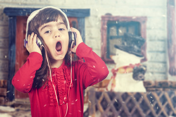 Adorable little girl wearing a Santa hat listening to music and singing Christmas carols. Cross...