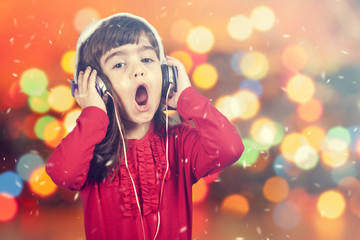 Portrait of a little Santa girl singing while listening to music. Defocused bokeh Christmas lights...