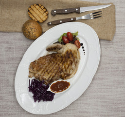 Juicy roast chicken with vegetables and ketchup. Served on porcelain plate on a tablecloth with fork and knife . Fried chicken tapaka, tobacco.