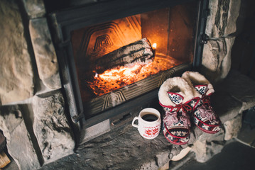 Christmas comfortable slippers by the warm cozy fireplace. Relaxing atmosphere in a chalet by authentic vintage fireside with a cup of hot drink. Winter and Christmas holidays concept