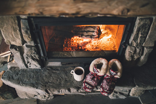 Christmas comfortable slippers by the warm cozy fireplace. Relaxing atmosphere in a chalet by authentic vintage fireside with a cup of hot drink. Winter and Christmas holidays concept