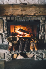 Winter boots in front of a fireplace. Family vintage folk boots drying near the fireside. Warm cozy fireplace in the authentic chalet. Hipster shoes getting warm near the burning fire in a cabin