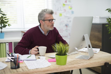 Man with cup of coffee working on computer.