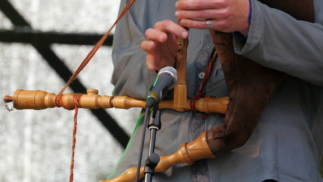 Playing the flute with other instruments on his neck. While playing the flute the man has other instruments hanging on his body they are wooden instruments just like a flute