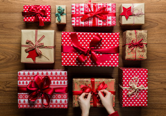 Woman fixing a bow on beautifuly wrapped vintage christmas presents on wooden background, view from above