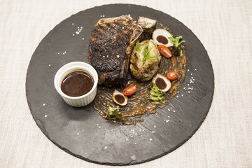 Ribeye steak from marble beef meat with vegetables and barbecue sauce. Served on a plate of black stone.