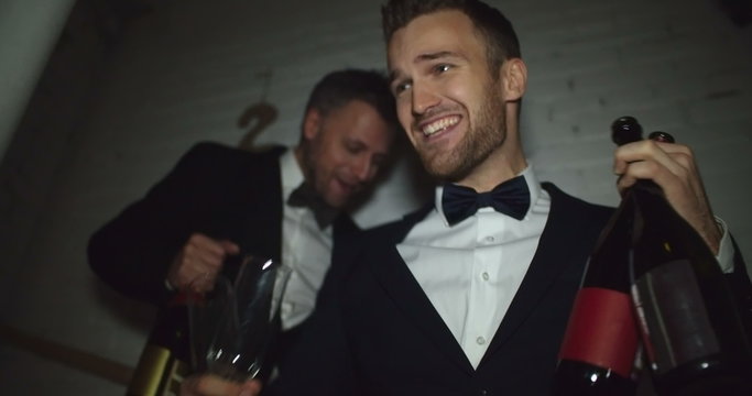 Two handsome guys going downstairs in nightclub with bottles of champagne