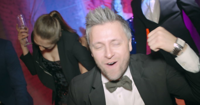 Group of friends are pushing a man sitting in office chair and drinking champagne