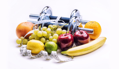 Chrome dumbbells surrounded with healthy fruits measuring tape on a  white background with shadows. Healthy lifestyle diet and exercise.