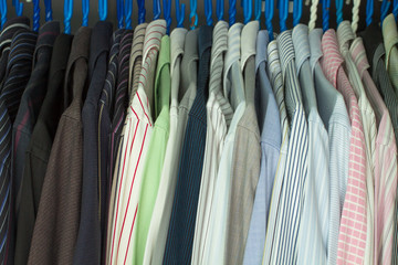 A collection of men's striped shirts, are hung orderly on a clothes rack of a closet.