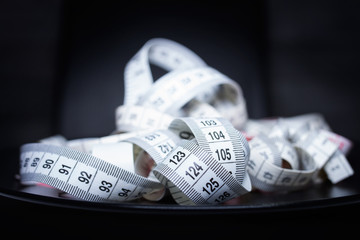 White measuring tape on a black plate, diet concept
