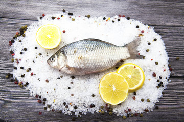 A  fresh carp live fish lying on a on salt and pepper background with slices of lemon and with salt dill. Live fish crucian Carassius auratus gibelio.