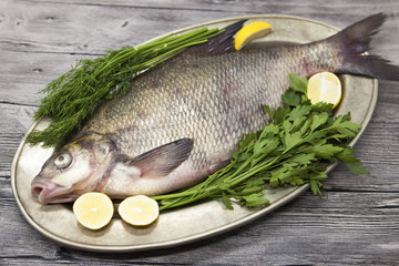 A large live bream river fish  fish lying on a on on an iron tray with a knife and slices of lemon and with salt dill