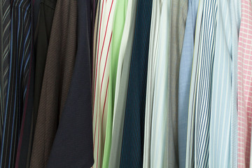 A collection of men's striped shirts, are hung orderly on a clothes rack of a closet.