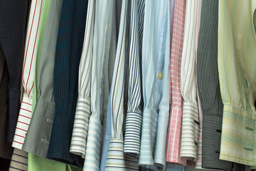 A collection of men's striped shirts, are hung orderly on a clothes rack of a closet.