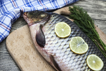 A large fresh carp live fish lying on a wooden board with a knife and slices of lemon and with salt dill.