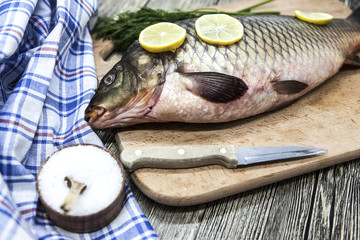 A large fresh carp live fish lying on a wooden board with a knife and slices of lemon and with salt dill.