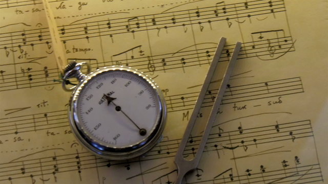 A clock and a metal on top of a music sheet. The circle thing is like a clock along side the metal object