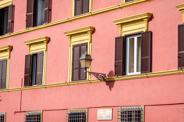 Metal lantern vintage retro street lighting on the facade of the house with windows are closed shutters and blinds on a sunny day on the streets of Rome, capital of Italy