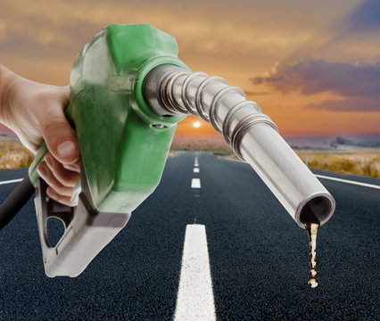 Male hand holding gas pump with one last drop and the road on the background