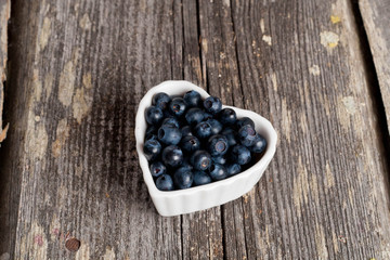 Heart shaped bowl of blueberries on wooden table
