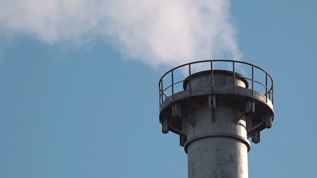 Industrial chimney flue gas detail with white smoke, blue winter sky in background