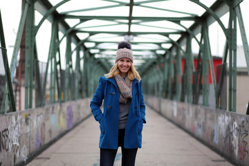 Blonde woman in blue coat and bobble hat on a bridge