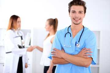 Attractive male doctor in front of medical group, crossed arms