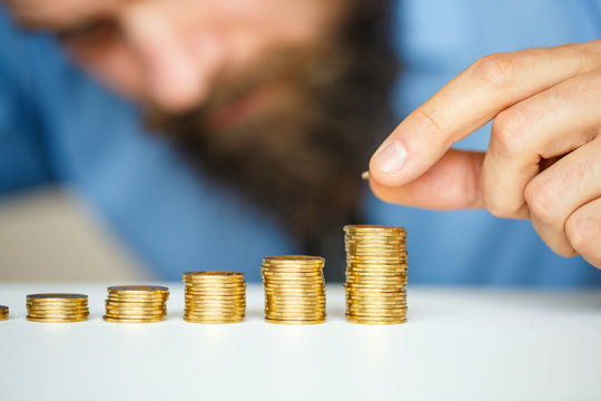 Male hand stacking gold coins into increasing columns