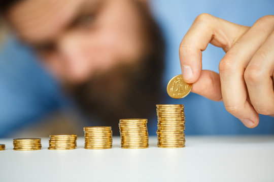 Male hand stacking gold coins into increasing columns