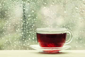 Cup of hot black tea on the blurred background of wet window on